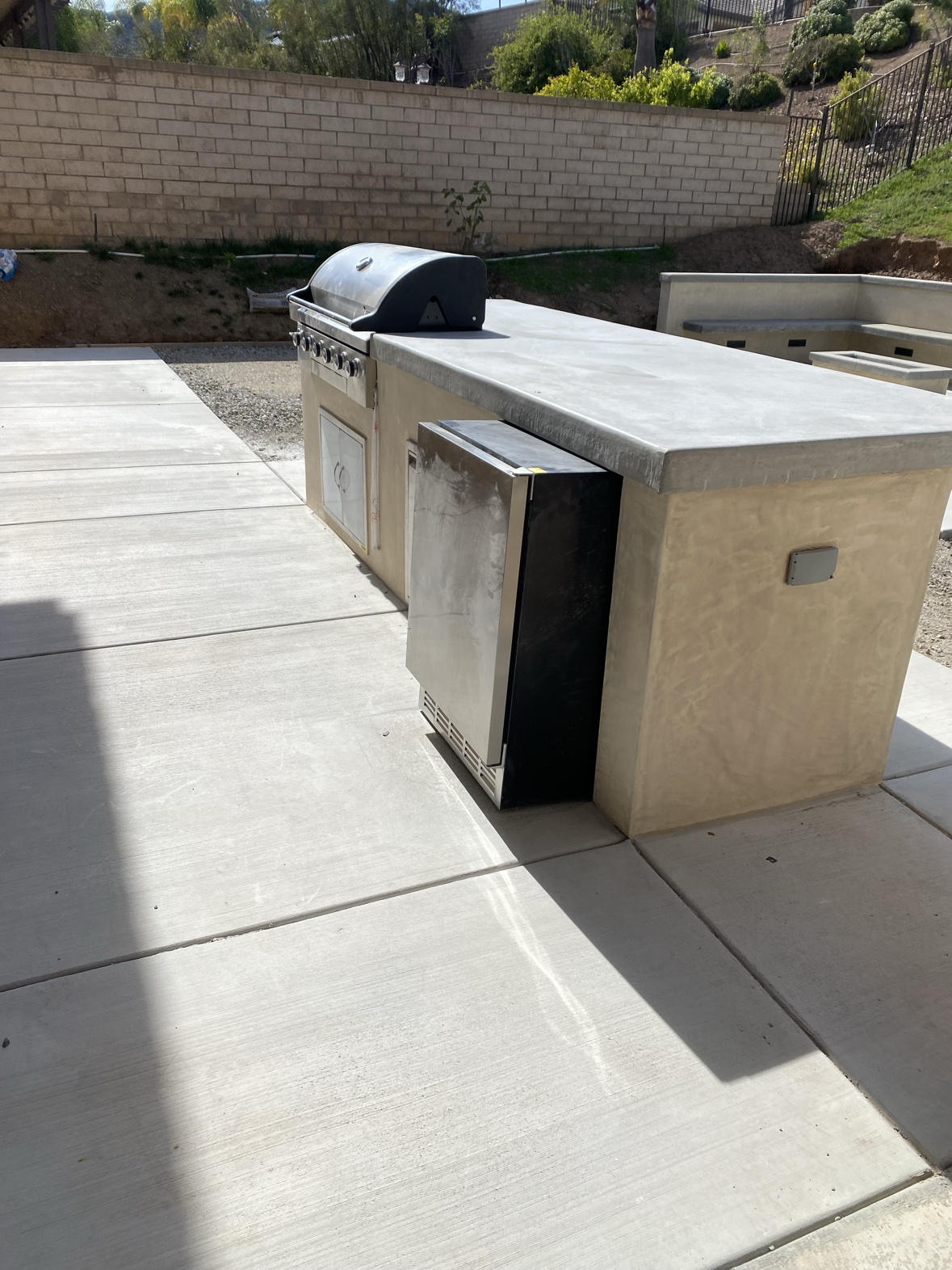 Backyard concrete patio with outdoor kitchen island, fire pit, and seat walls
